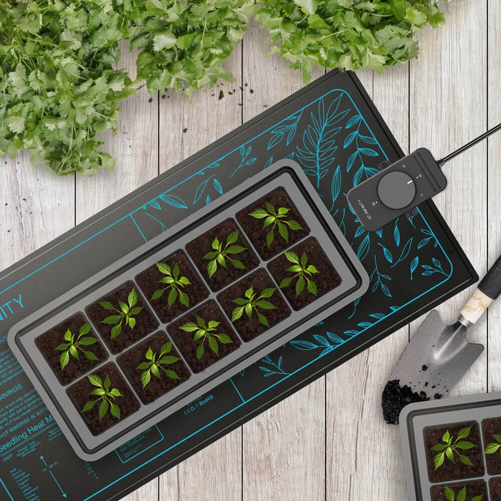 Small plants in a grow tray on top of Suncore S3 seedling heat mat on a wooden surface with gardening tools.