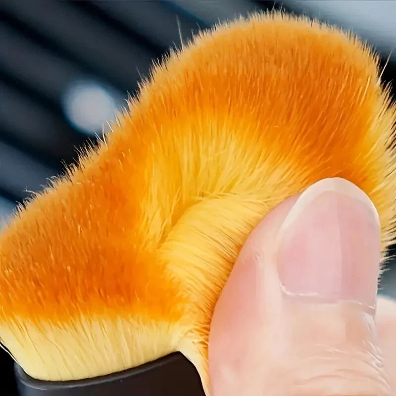 Close-up of auto detail brush with soft fine orange bristles held by a hand.