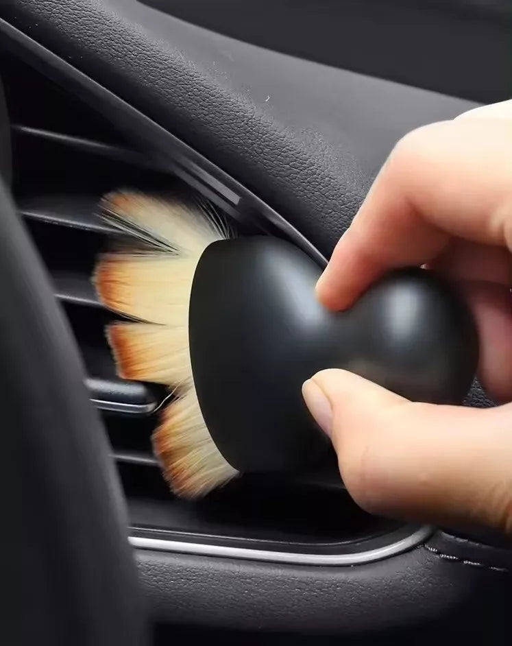Hand using a car air vent cleaning brush to clean a car's air vent.