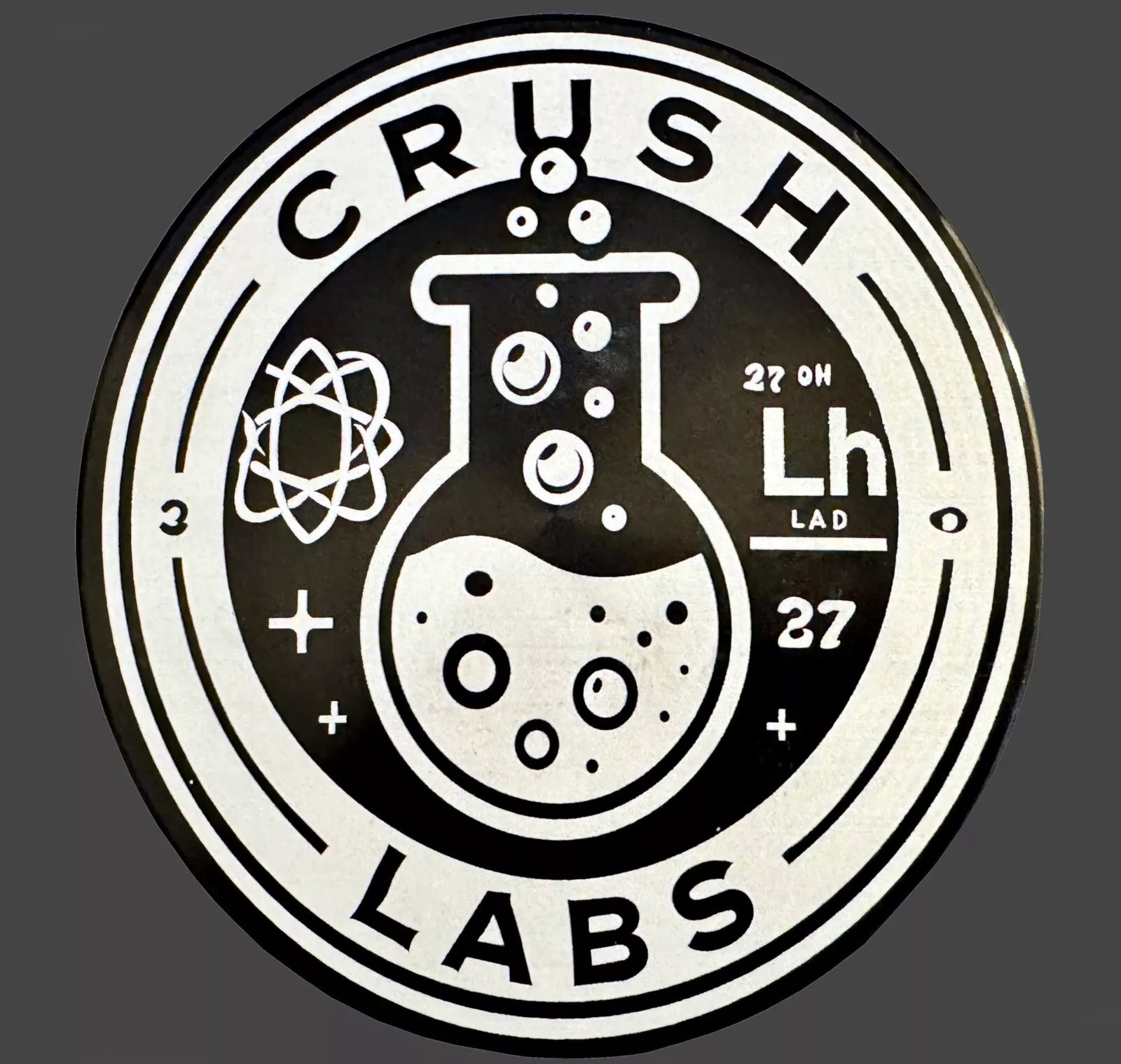 Logo of Crush Labs on grinder lid with a beaker and atom symbol on a dark background