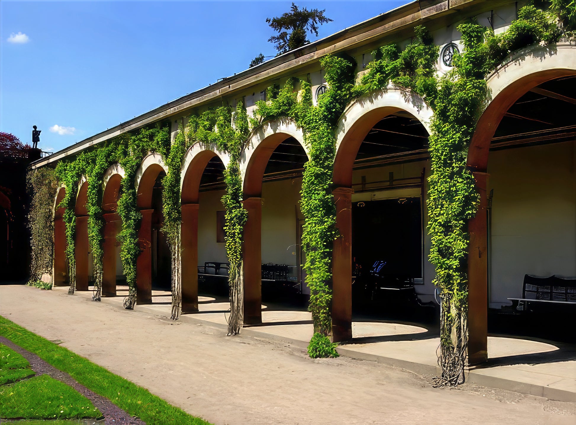 Long building with arches covered in green Chocolate vine under a clear blue sky.