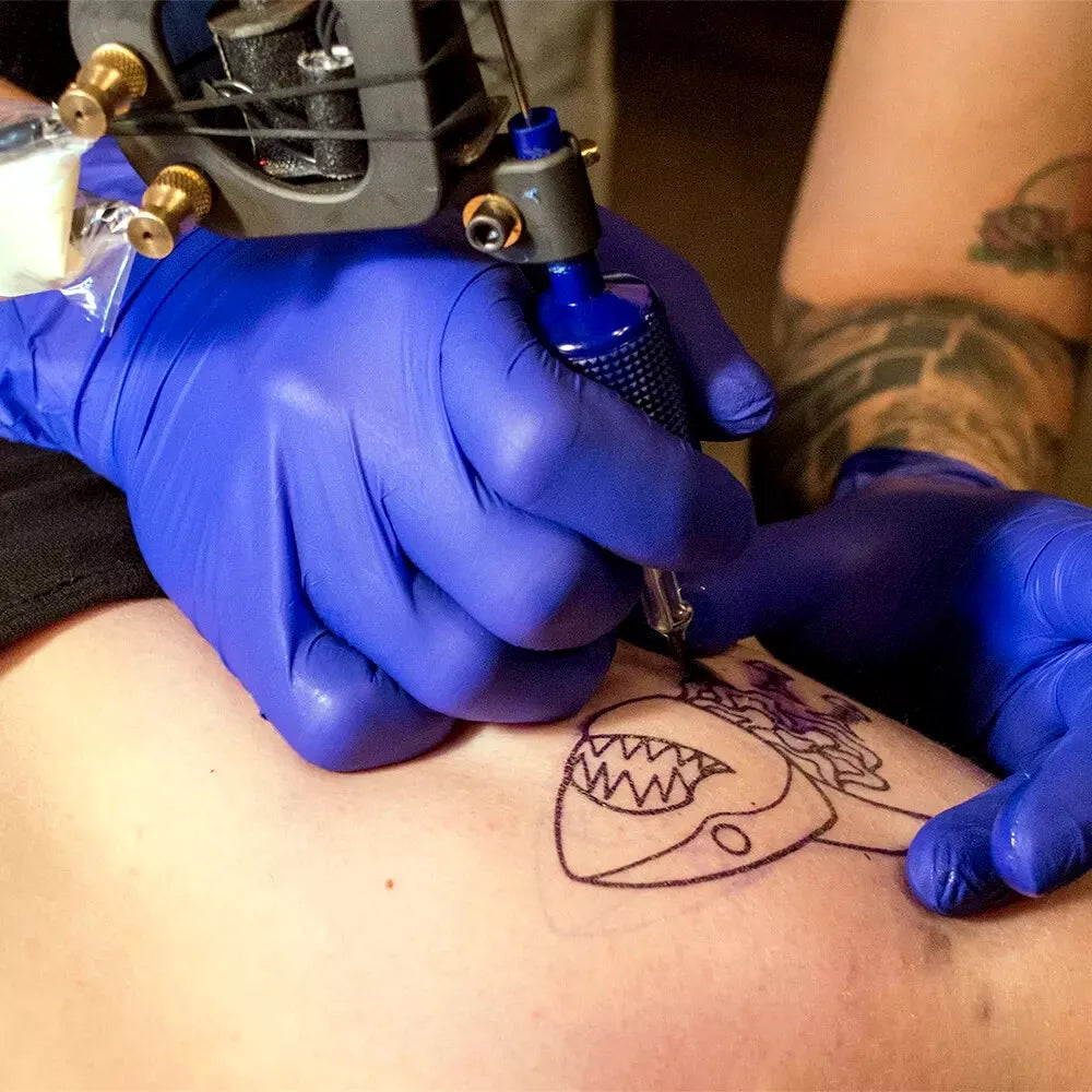 Tattoo artist in blue nitrile gloves working on a tattoo with a shark design.