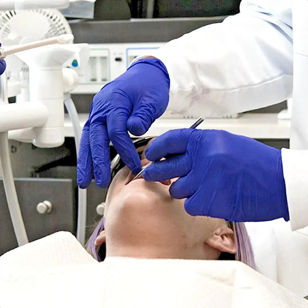 Person receiving dental treatment with indigo blue nitrile exam gloves in a clinical setting