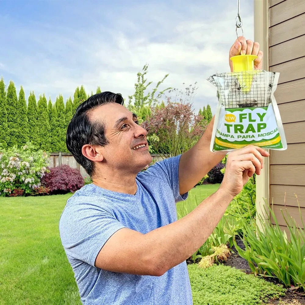 Man hanging a fly trap in a garden behind house.