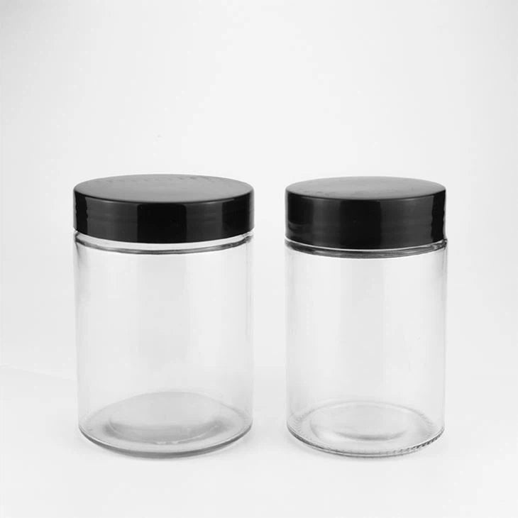 Two clear glass jars with black lids on a white background