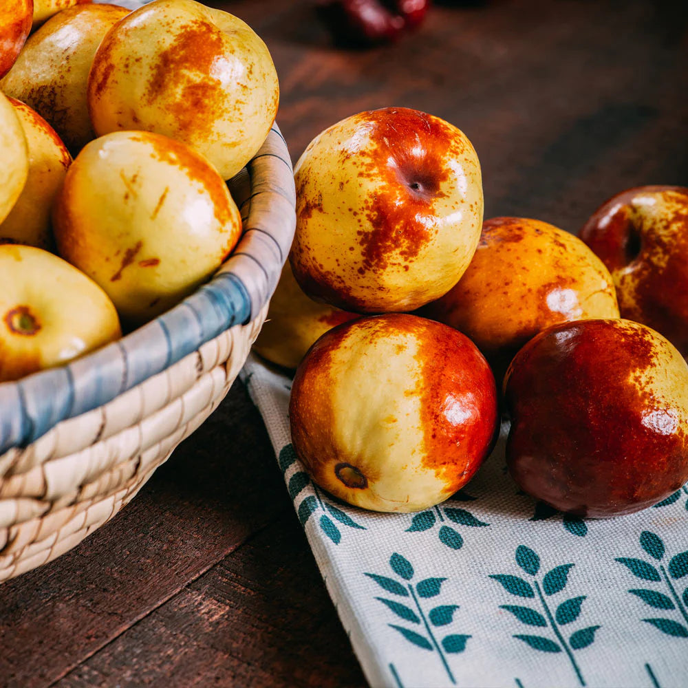 Basket and pile of red and yellow Jujube fruits on a wooden surface with a patterned cloth.