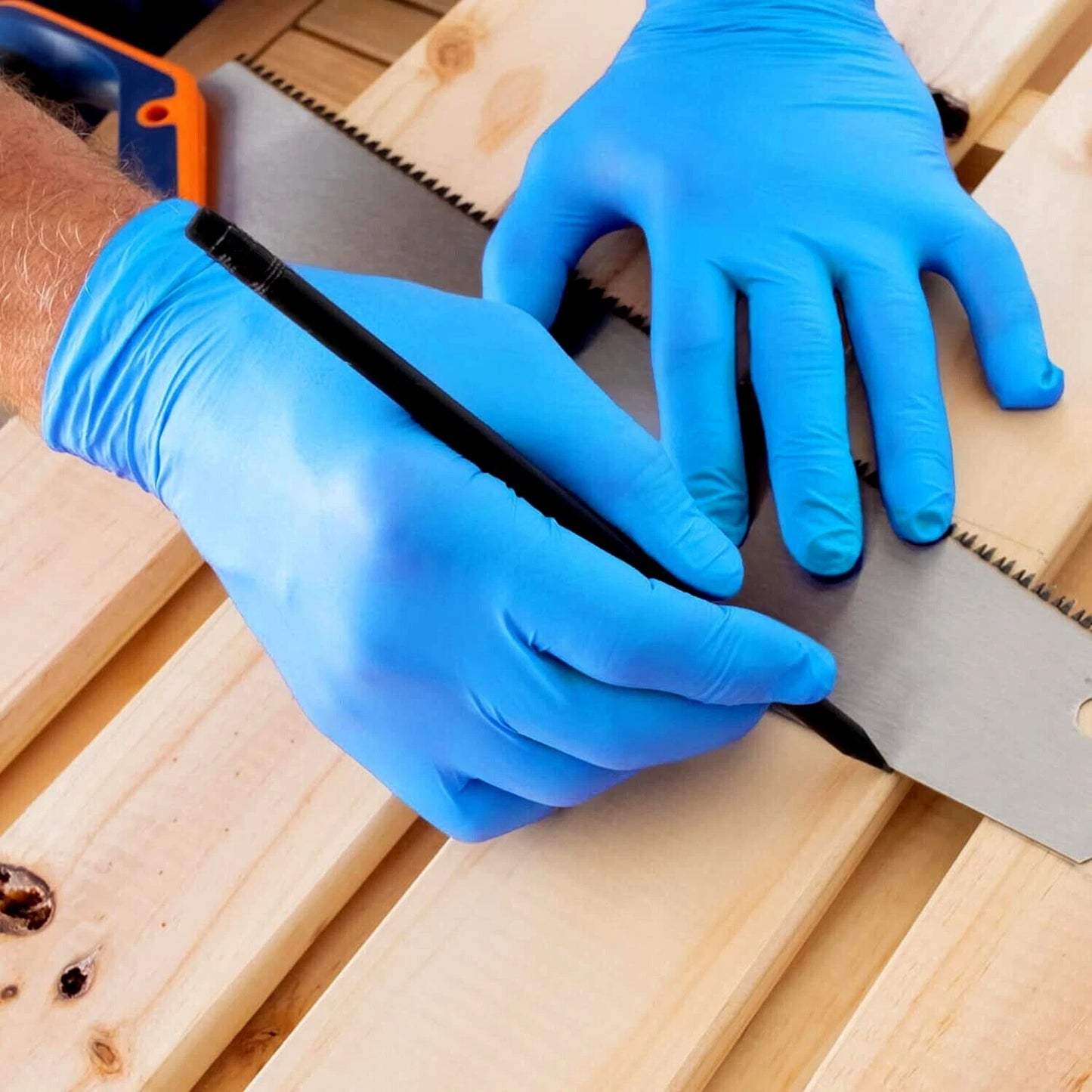 Person wearing blue gloves using a saw on wooden planks