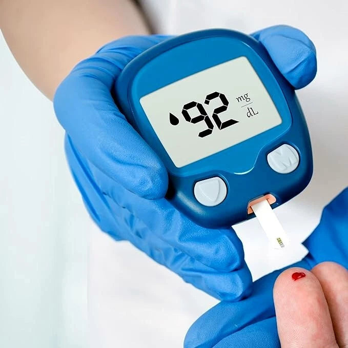 Person wearing blue nitrile exam gloves using a blue blood glucose meter on a white background