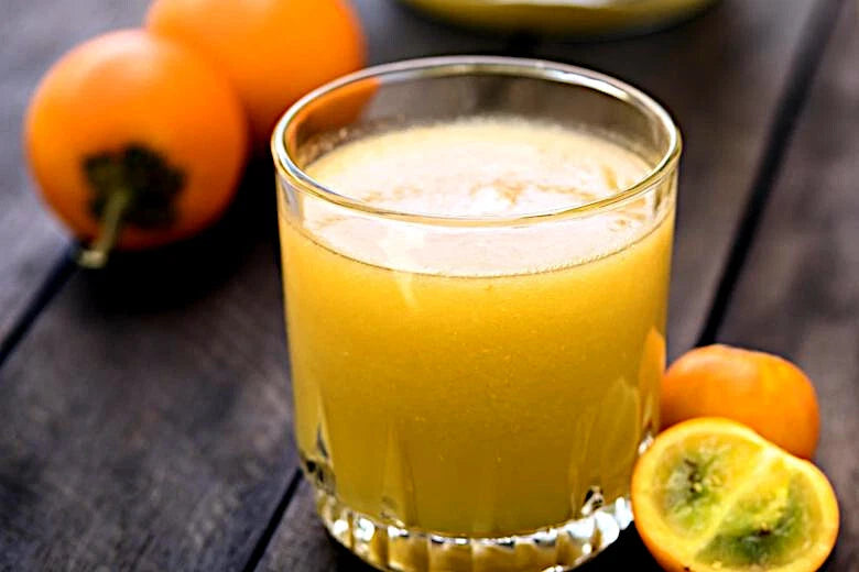 Glass of naranjilla orange juice with oranges on a wooden surface