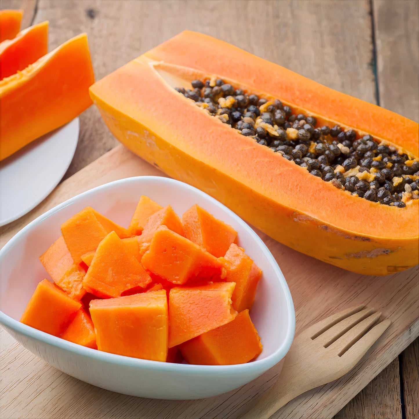 Dwarf Hawaiian Solo Sunrise Papaya cut in half with seeds on a wooden table, next to a bowl of chopped papaya pieces.