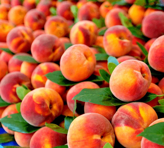 Stack of nemaguard peaches with green leaves on a blue cloth