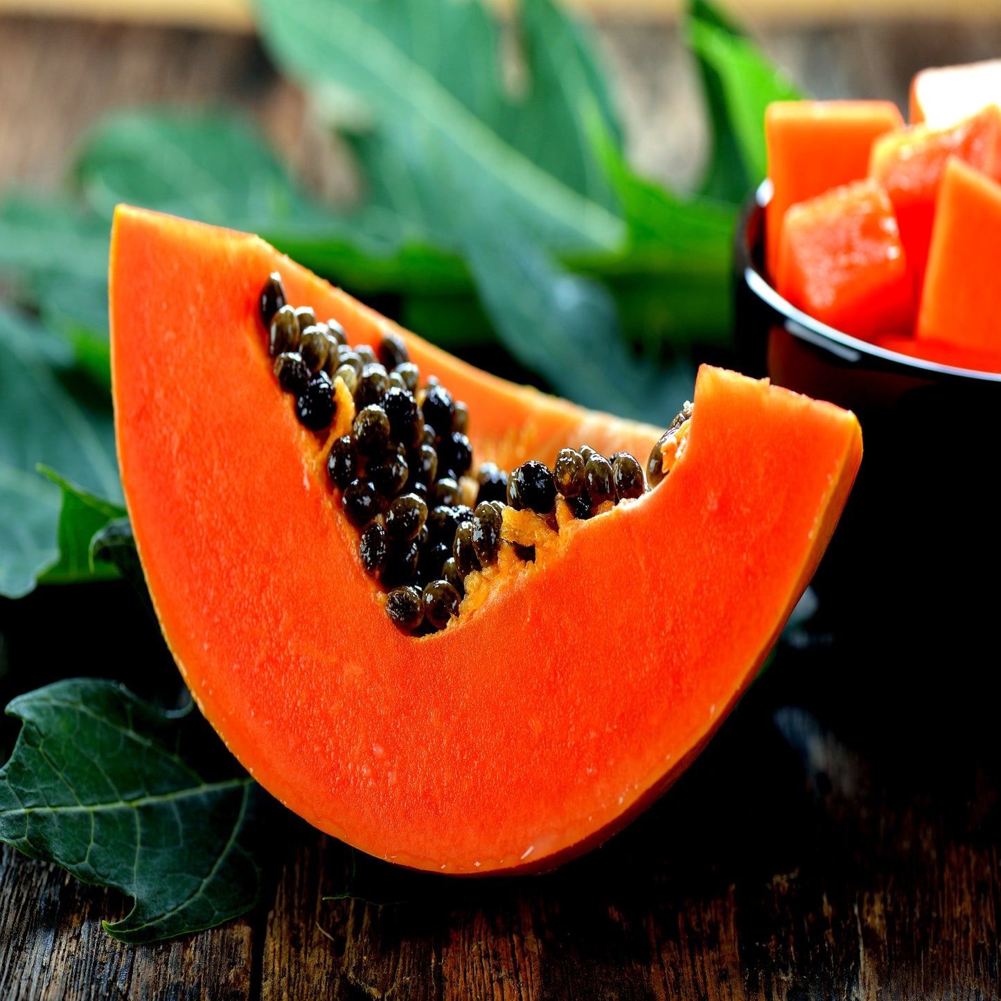 Sliced papaya on a wooden surface with green leaves in the background