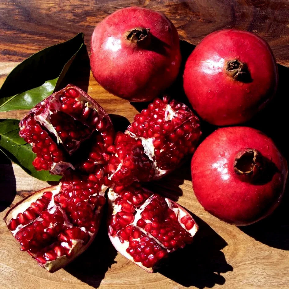 Pomegranates on a wooden surface with one cut open to reveal seeds.