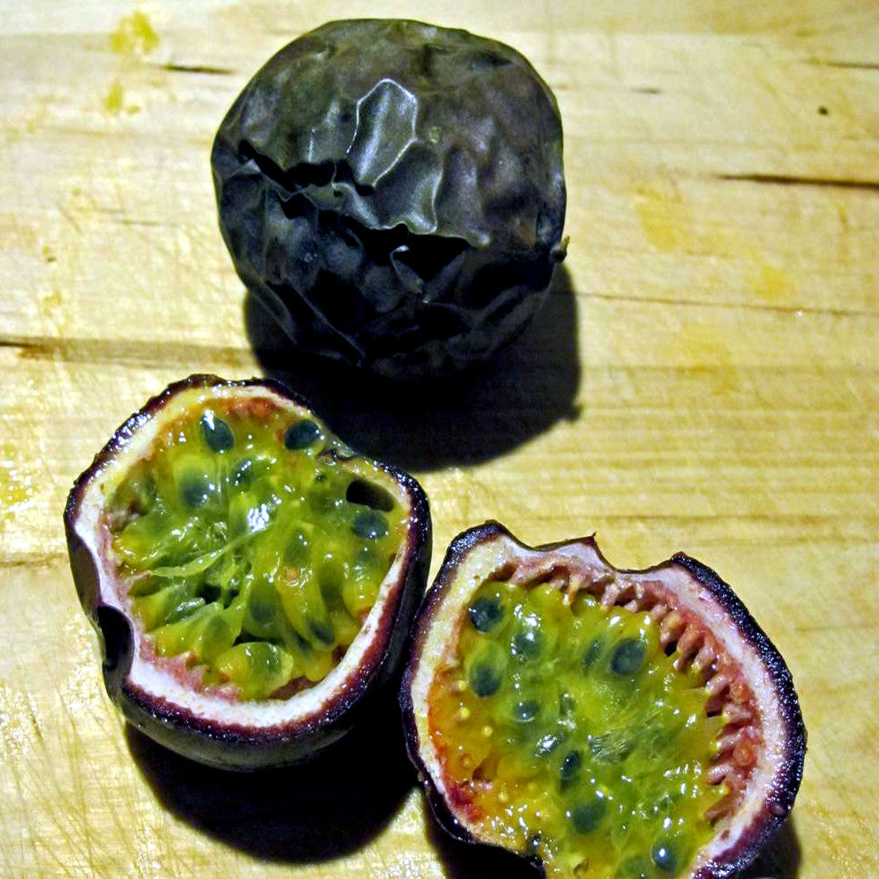Purple passionfruit split in half with yellow fruit lying on wooden table. 