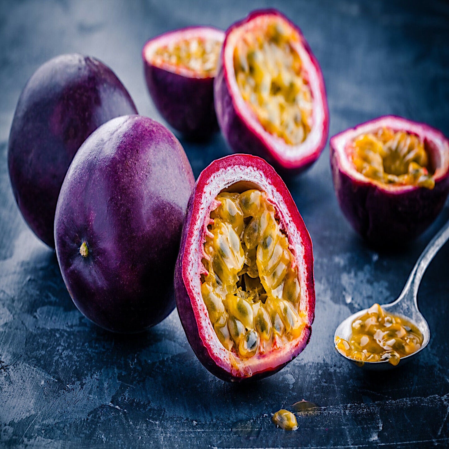 Purple passionfruit with one split in half with a spoonful of fruit lying on dark table.  Passiflora edulis