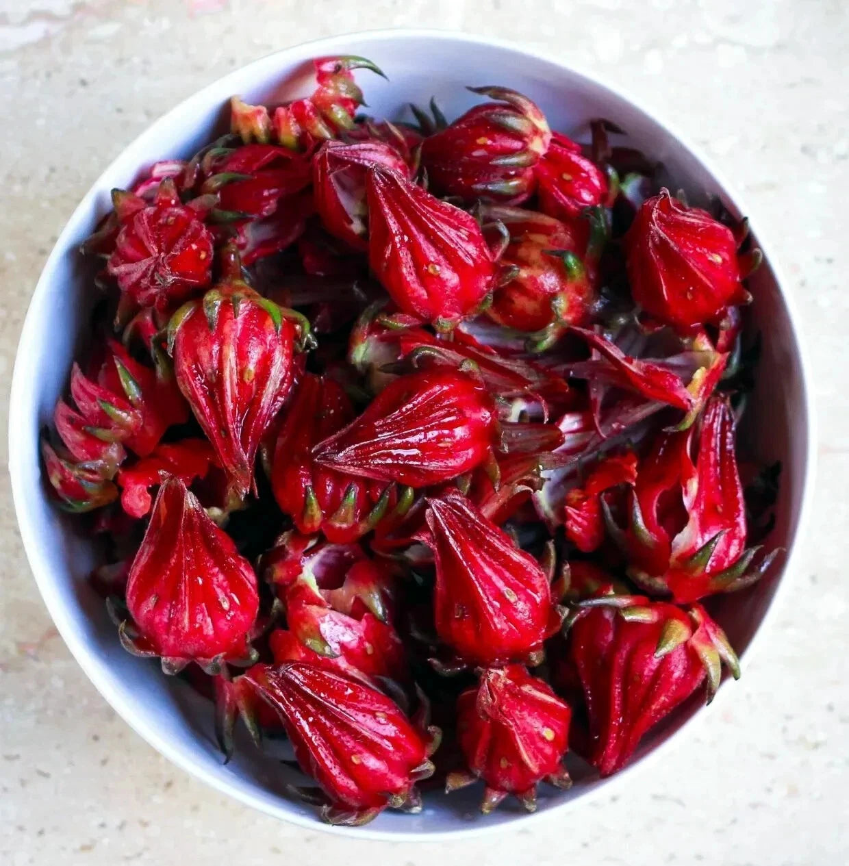 Red Roselle hibiscus flowers in a white bowl on a light background