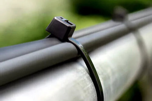 Close-up of a heavy duty 24 inch black nylon  cable tie securing large wires to metal piping.