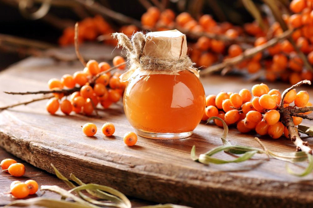 Glass jar of Sea Buckthorn juice with sea buckthorn berries on a wooden surface