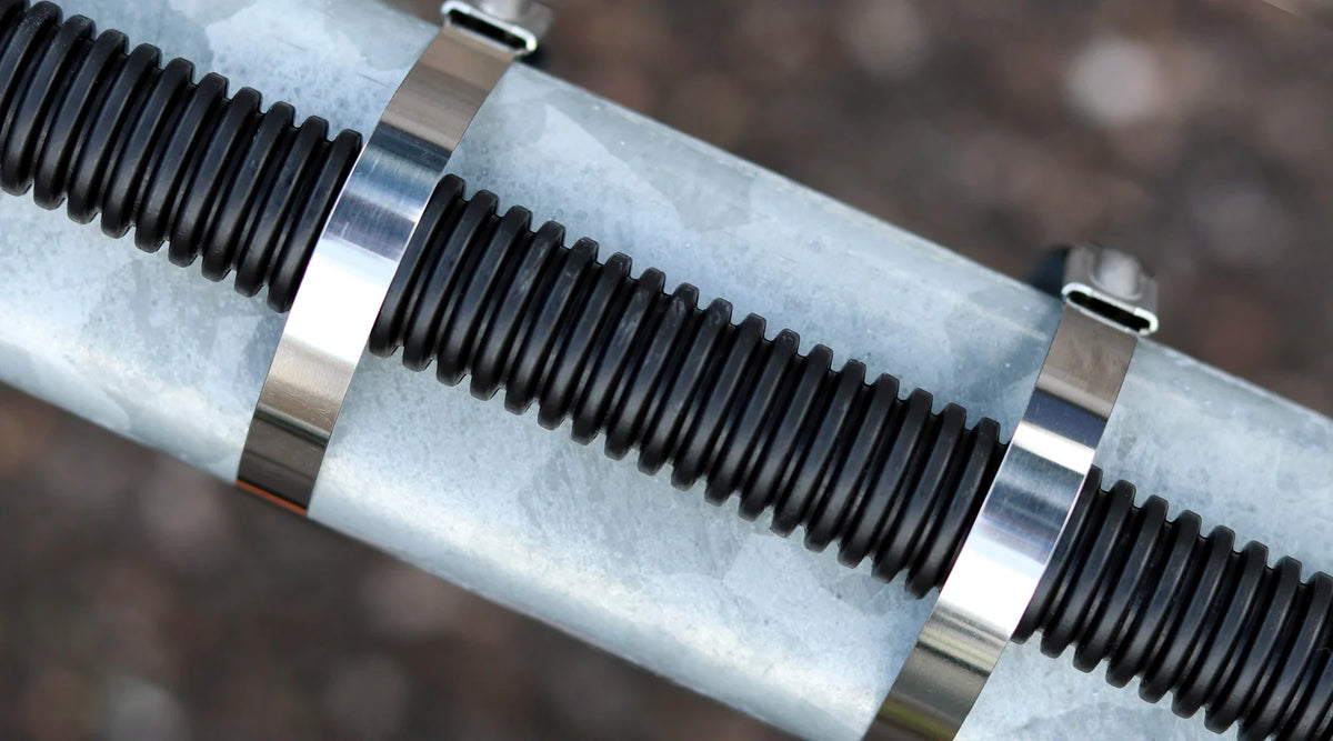 Close-up of a metallic silver cylindrical component with black ribbed bands secured by shiny silver 304 stainless steel zip ties, set against a blurred brown outdoor background.
