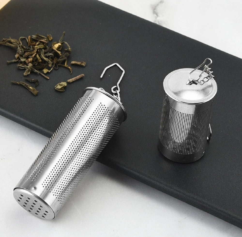 Stainless steel tea infusers on a black tray with dried tea leaves