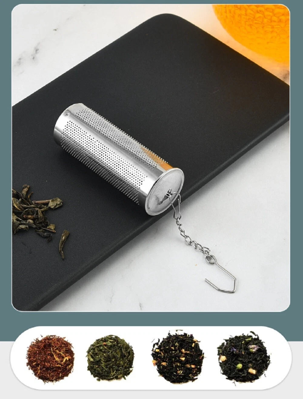 Silver stainless steel tea infuser on a black tray with dried tea leaves and a marble background