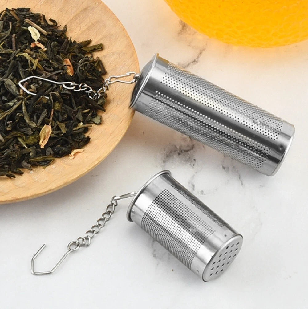 Two stainless steel tea infusers on a marble surface with a wooden bowl of loose tea leaves.