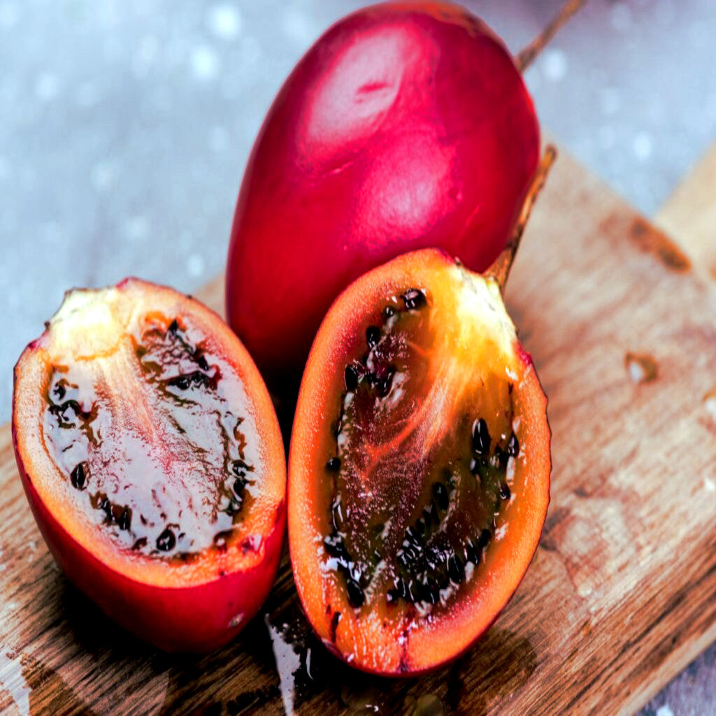 Red Tamarillo Tree Tomato fruit, possibly a passion fruit, cut in half on a wooden surface with a blurred background. Solanum betaceum