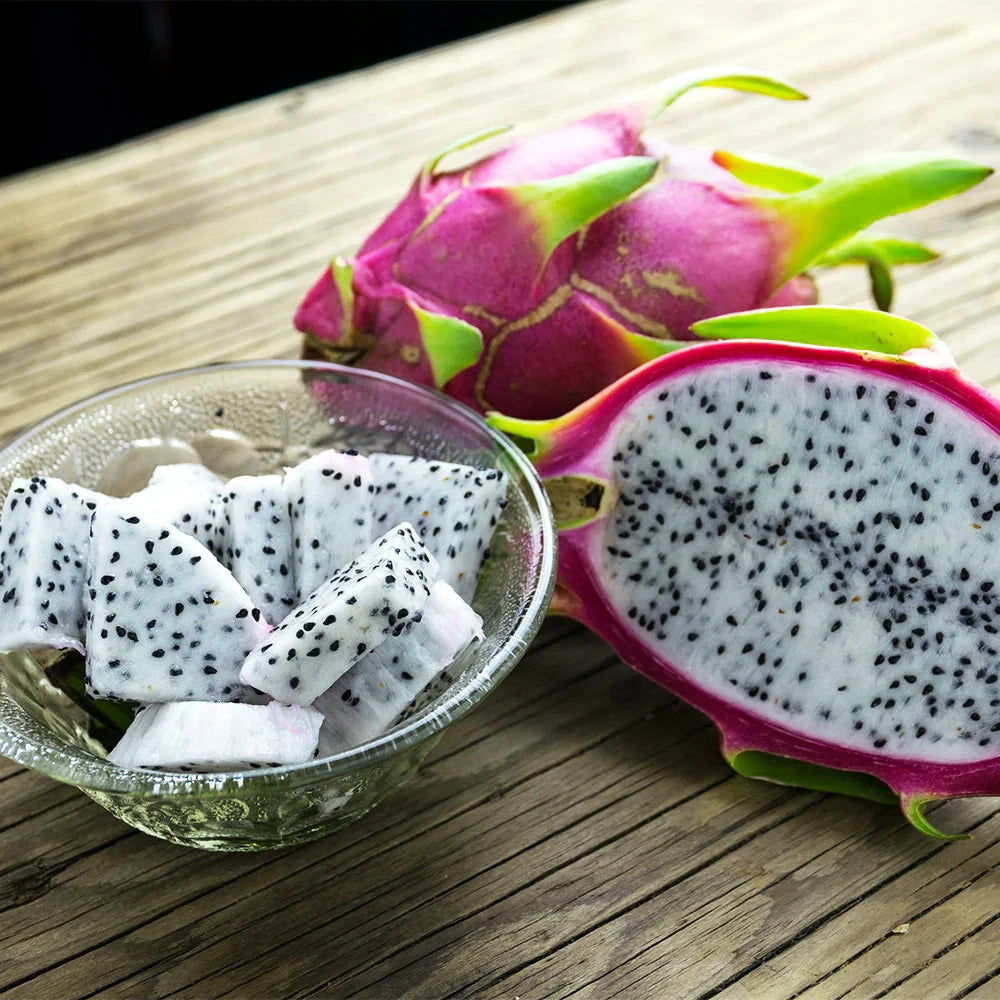 White dragon fruit cut in half with bowl of cut white fruit with black seeds on wood table. Pitaya (Hylocereus undatus)