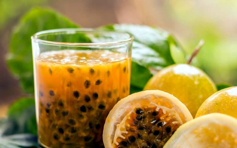 Glass of Yellow Passion fruit juice with passion fruits and leaves in the background